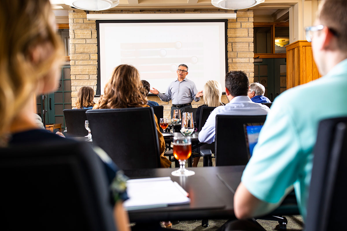 A man giving a presentation to a group of people with attendees having drinks