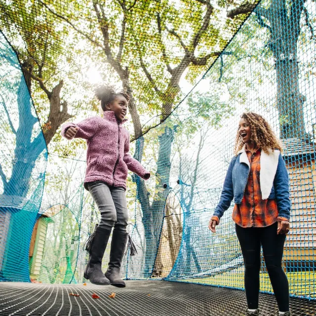 Mom and daughter jumping on a trampoline, captured mid-air with smiles on their faces.