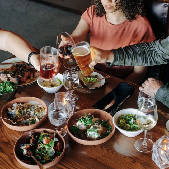 A table filled with various dishes and drinks, as friends raise their glasses for a toast during a lively dining experience.