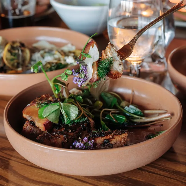 A rustic bowl of gourmet food featuring seared meat, fresh greens, and edible flowers.