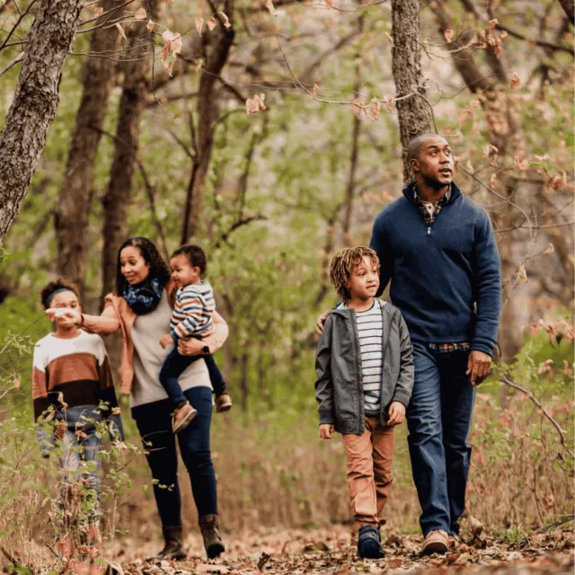 Family hiking in the woods during the fall or winter. They are all wearing long sleeves and pants.