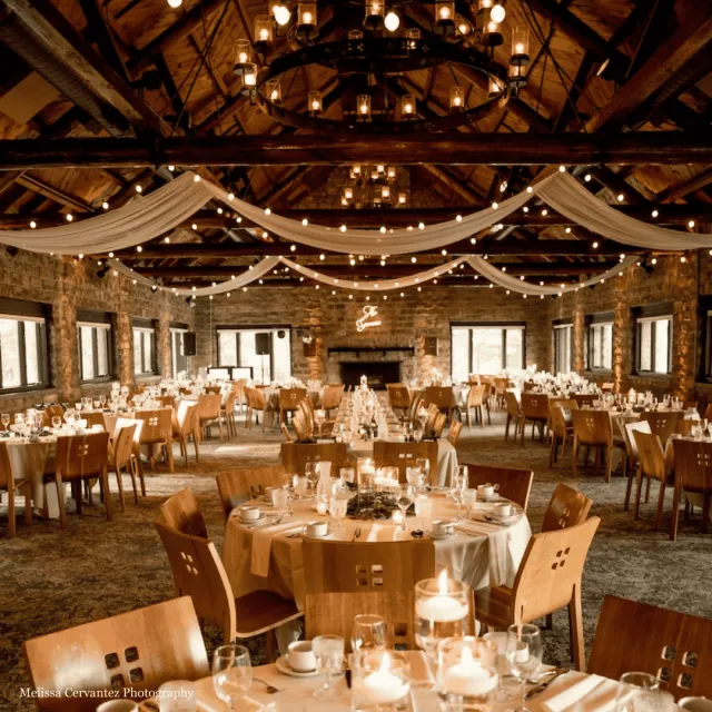 Rustic interior wedding venue with chandeliers and drapes hanging from the ceiling. 