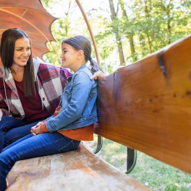 Mother and daughter sitting on a wooden bench in the outdoors.