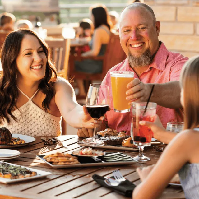 Family dining outside on a patio in warm weather clinking their drinks together.