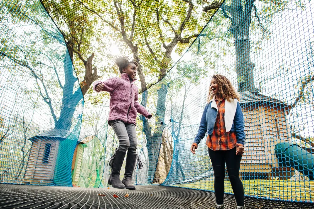 Mom and daughter jumping on a trampoline, captured mid-air with smiles on their faces.