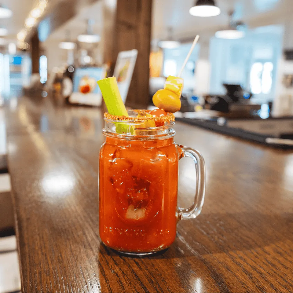 Bloody Mary sitting on an empty bar top garnish with olives and celery.
