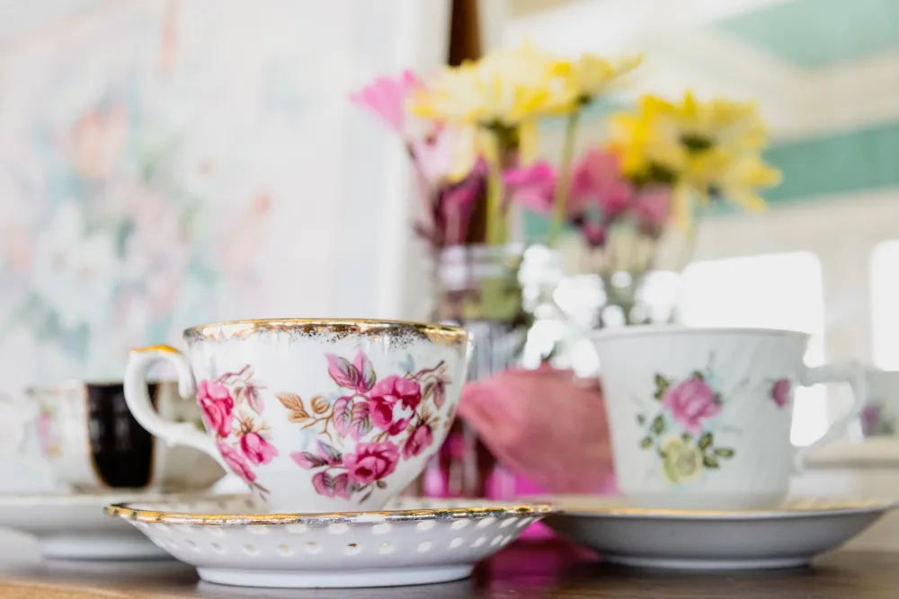 Floral tea cup sitting on a table with flowers blurred in the background.