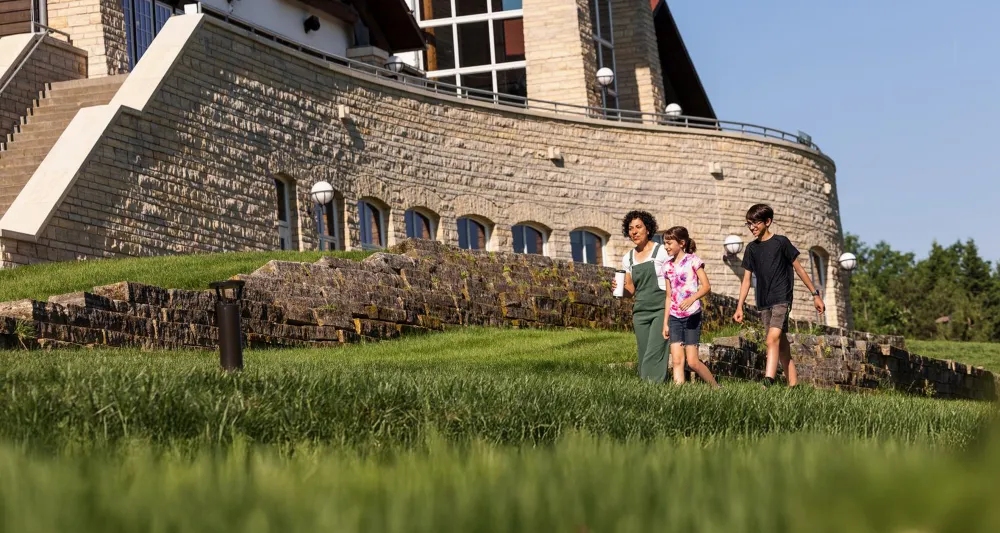 A mother and two kids walk up a grassy path toward Lied Lodge on a sunny summer day.