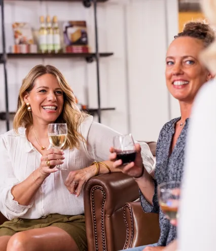 Two women relax on a couch, each holding a wine glass, enjoying a cozy moment together.