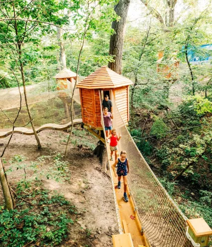 A wooden treehouse nestled among lush green trees, surrounded by nature and sunlight filtering through leaves.