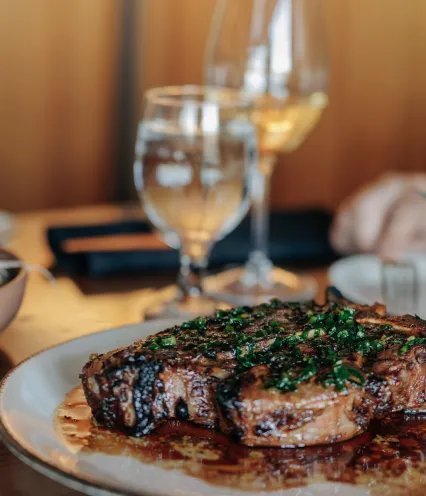A juicy steak garnished with fresh herbs, served on a plate with wine and water glasses in a cozy dining setting.
