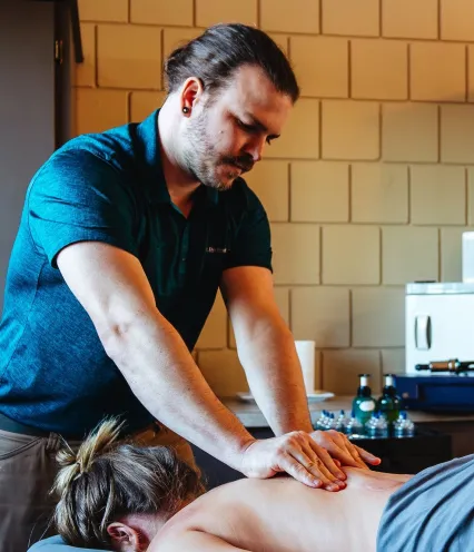 A person receiving a massage while lying face down on a massage table, with a therapist applying pressure on their back.