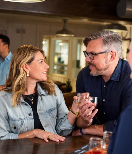 A lively bar scene with two people engaged in conversation, holding drinks; others socialize in the background.