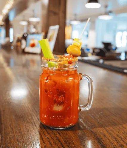 Bloody Mary sitting on an empty bar top garnish with olives and celery.