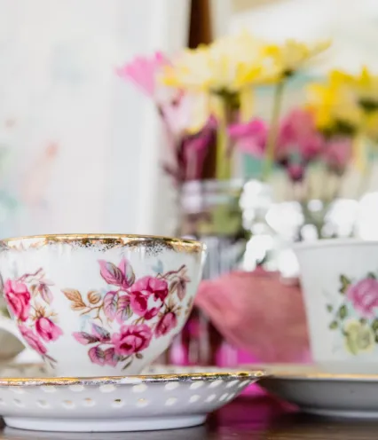 Floral tea cup sitting on a table with flowers blurred in the background.