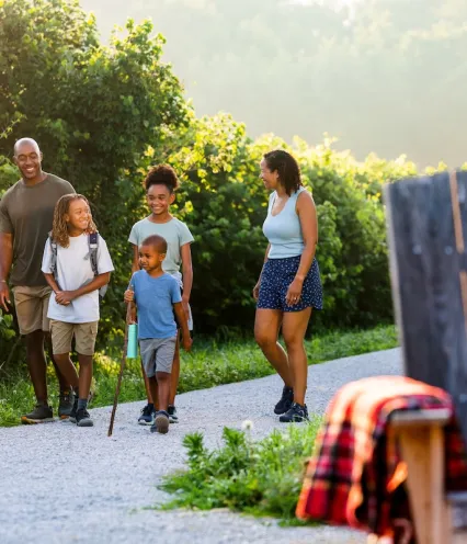 Family in short sleeves and shorts walking on an outdoor gravel path surrounded by greenery.