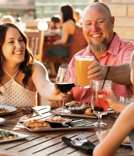 Family dining outside on a patio in warm weather clinking their drinks together.