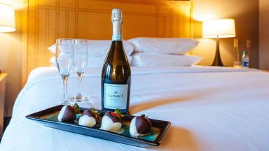 A bottle of champagne and two wine glasses elegantly placed on a neatly made bed.