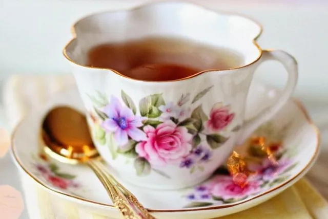Elegant floral teacup filled with tea, resting on a saucer with a golden spoon beside it, exuding vintage charm.
