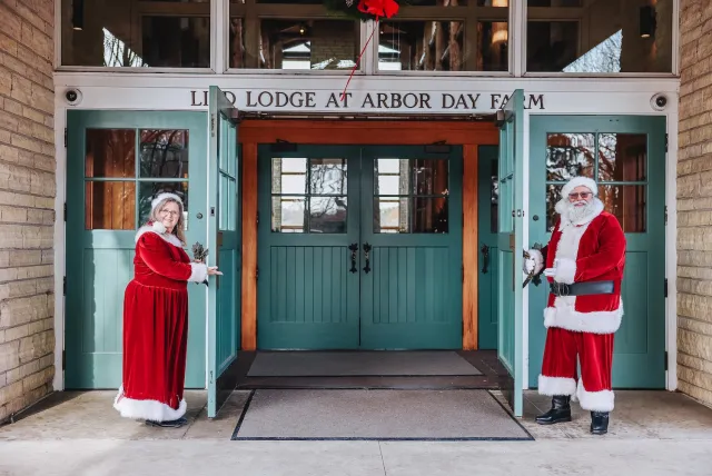 A festive scene at Arbor Day Farm Lodge features a Santa and Mrs. Claus at the entrance, warmly welcoming visitors.