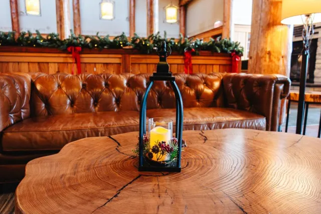 A cozy lounge with a brown leather sofa, a rustic wooden coffee table, and a lantern centerpiece featuring a lit candle and greenery.