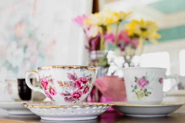 Floral tea cup sitting on a table with flowers blurred in the background.