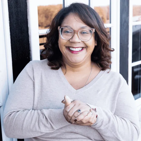 Headshot of an employee leaning against the outside of a building with windows and white trim.