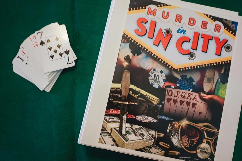 A deck of cards and a binder with 'Murder in Sin City' written on it on a green background.