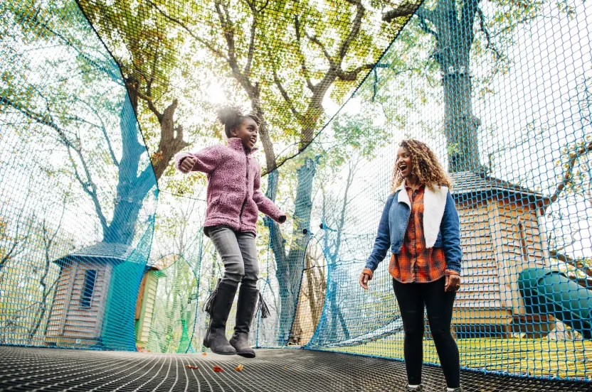 Mom and daughter jumping on a trampoline, captured mid-air with smiles on their faces.