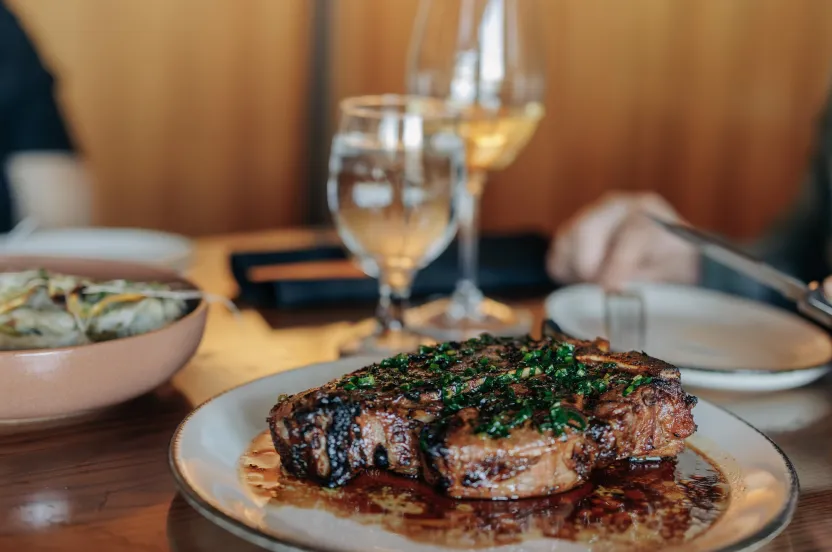 A juicy steak garnished with fresh herbs, served on a plate with wine and water glasses in a cozy dining setting.