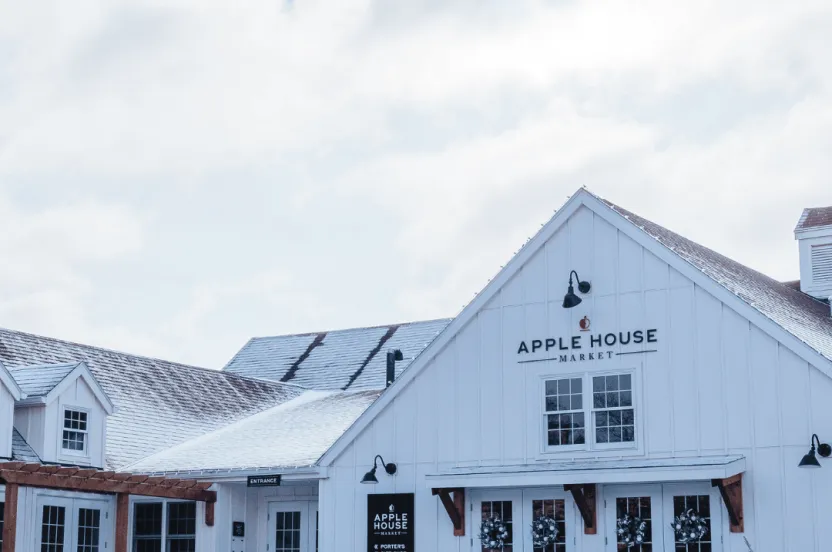 Exterior view of the Apple House Market, a modern white barn-style building with snow on the roof and ground.