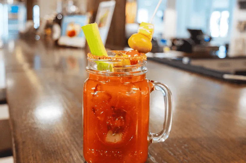 Bloody Mary sitting on an empty bar top garnish with olives and celery.