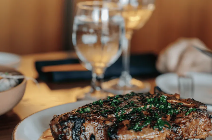 Large steak setting on a dinner plate with two wine glasses faded in the background.