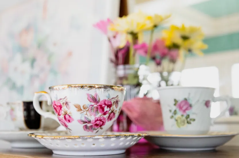 Floral tea cup sitting on a table with flowers blurred in the background.