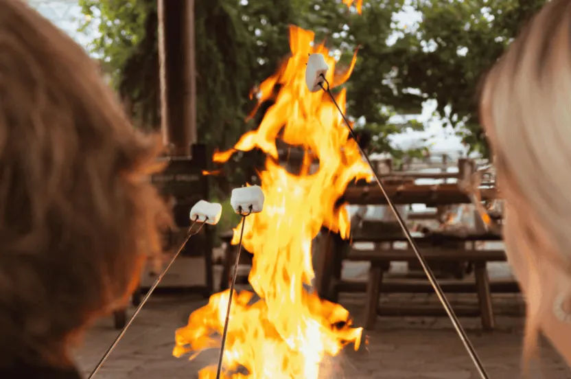 People sitting outdoors roasting marshmallows over a fire.
