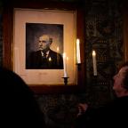 Woman holding candlestick looking at portrait on the wall in the dark.