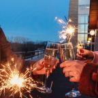 Two people clink champagne glasses, holding sparklers. It's dusk with a festive atmosphere, evoking celebration and joy against a building backdrop.