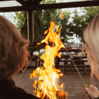 People sitting outdoors roasting marshmallows over a fire.