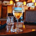 A glass of white wine on a wooden table in a restaurant setting with dim lighting and modern decor.